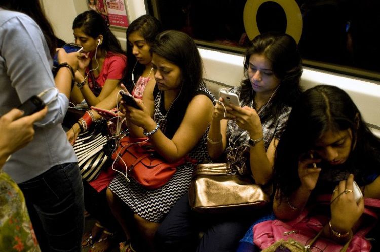 Indian women use their smartphones as they travel in the metro carriage reserved for women in New Delhi on July 14, 2015.  With the first stretch of metro inaugurated in the city in 2002, as of June 2015 the network consists of five regular lines and one express line covering 193 kms and 140 stations.  AFP PHOTO/ Anna ZIEMINSKI